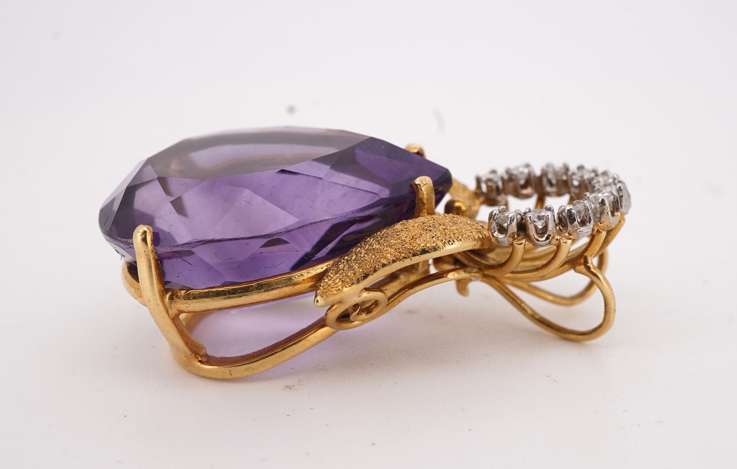 An Amethyst and diamond pendant, claw-set with a pear-shaped amethyst, topped with a foliate surmount in textured gold, accented with and arc of brilliant-cut diamonds totalling approximately 0.30 carats, length 3.5cm, s